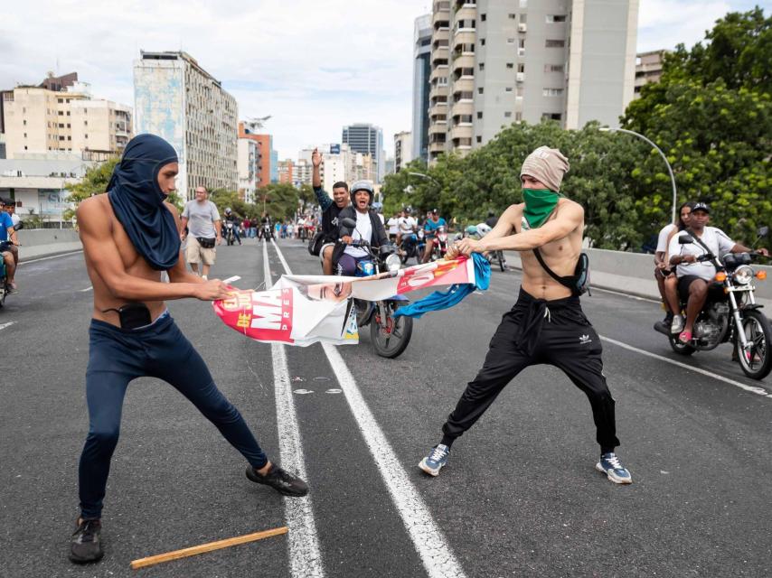 Dos manifestantes contrarios a la dictadura socialista venezolana intentar romper un cartel electoral de Nicolás Maduro.