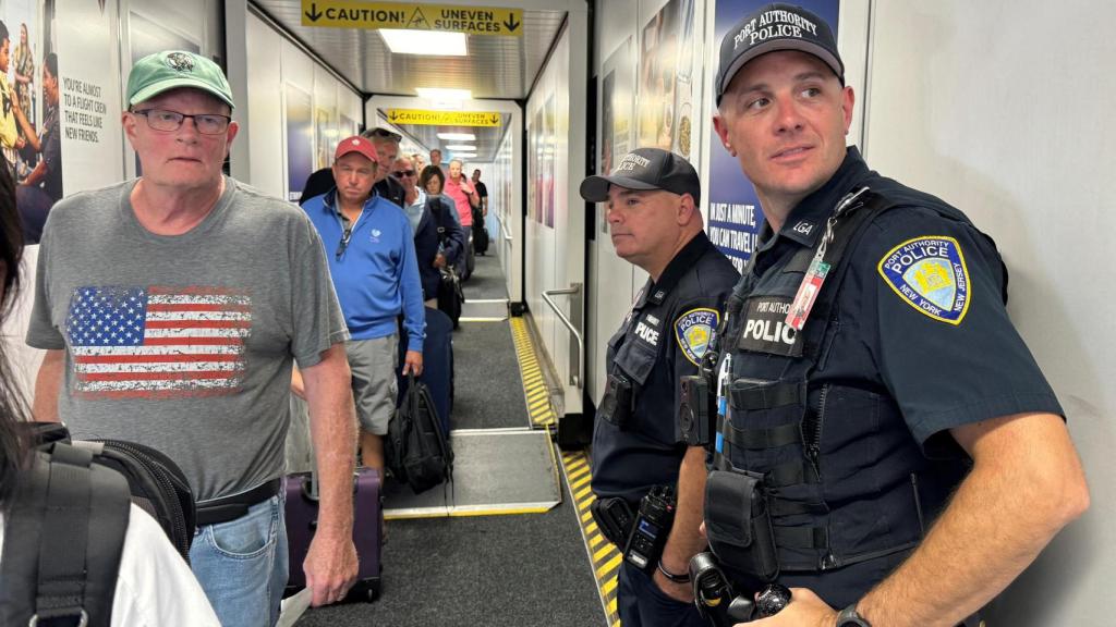 Oficiales de la Aduana de Nueva York hacen guardia mientras la gente accede a un avión