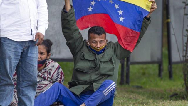 Un migrante venezolano permanece en condición de refugiado mientras alza su bandera.