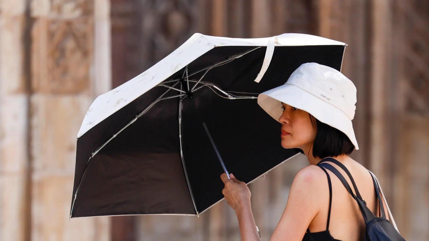 Una turista se protege del calor con parasol mientras pasea.