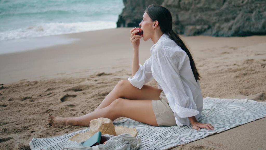 Una mujer comiendo una pieza de fruta en la playa.