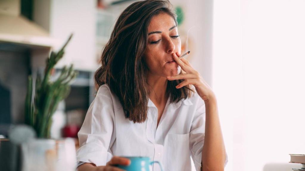 Mujer fumando mientras lee y toma café.