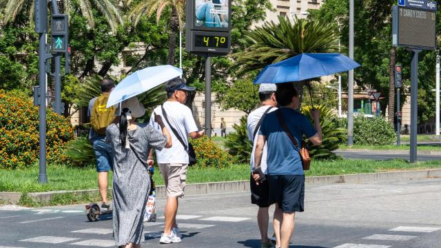 Varias personas al lado de un termómetro en las calles de la capital hispalense a 47 grados de temperatura.