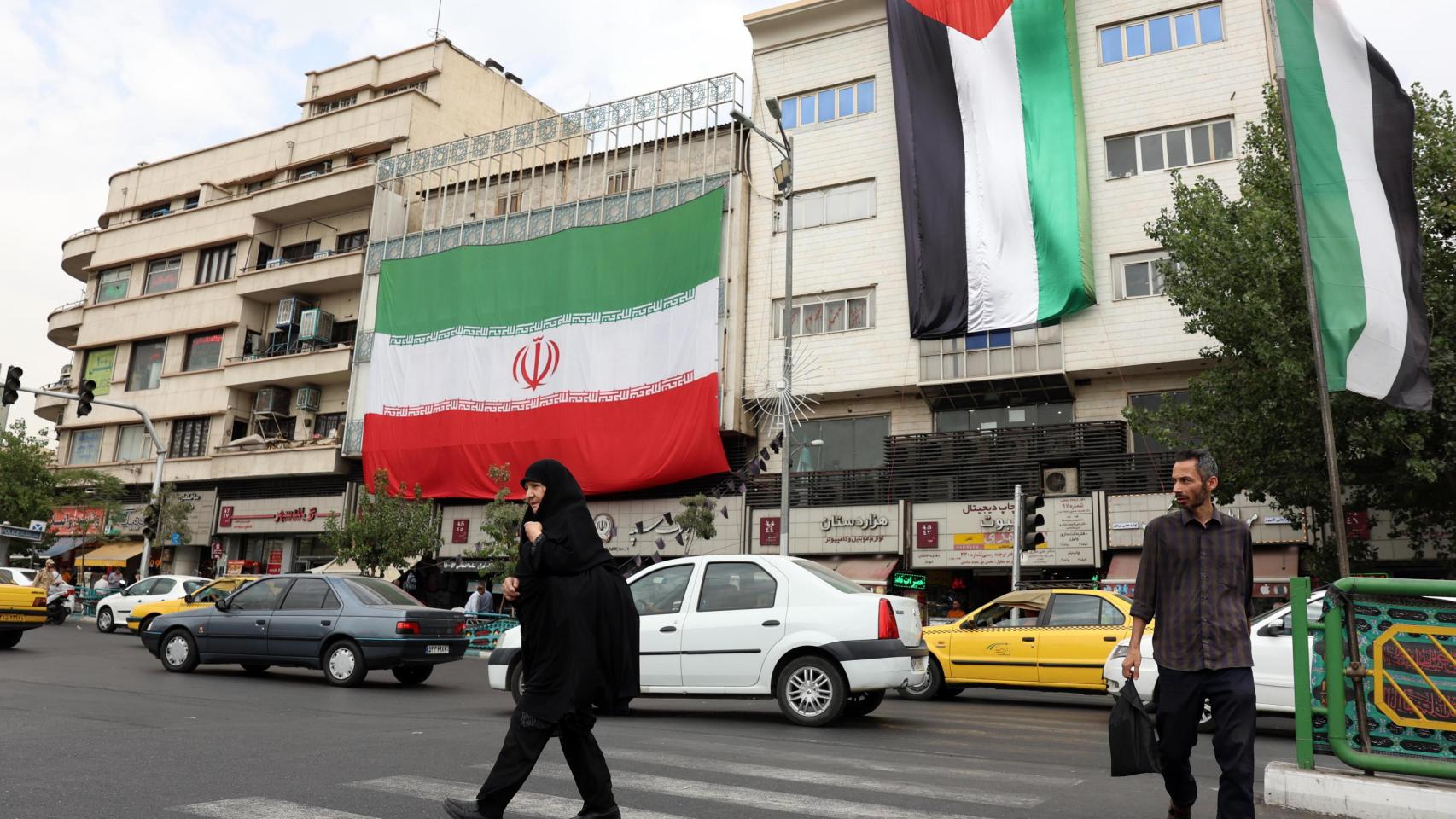 Dos hombres caminan junto a un edificio con la bandera iraní y palestina en Teherán.