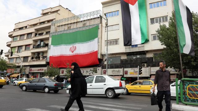 Dos hombres caminan junto a un edificio con la bandera iraní y palestina en Teherán.