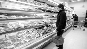 Un joven frente al estante de la carne en un supermercado español.