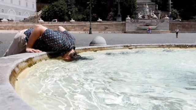 Una mujer sumerge su cabeza en el agua de una fuente.