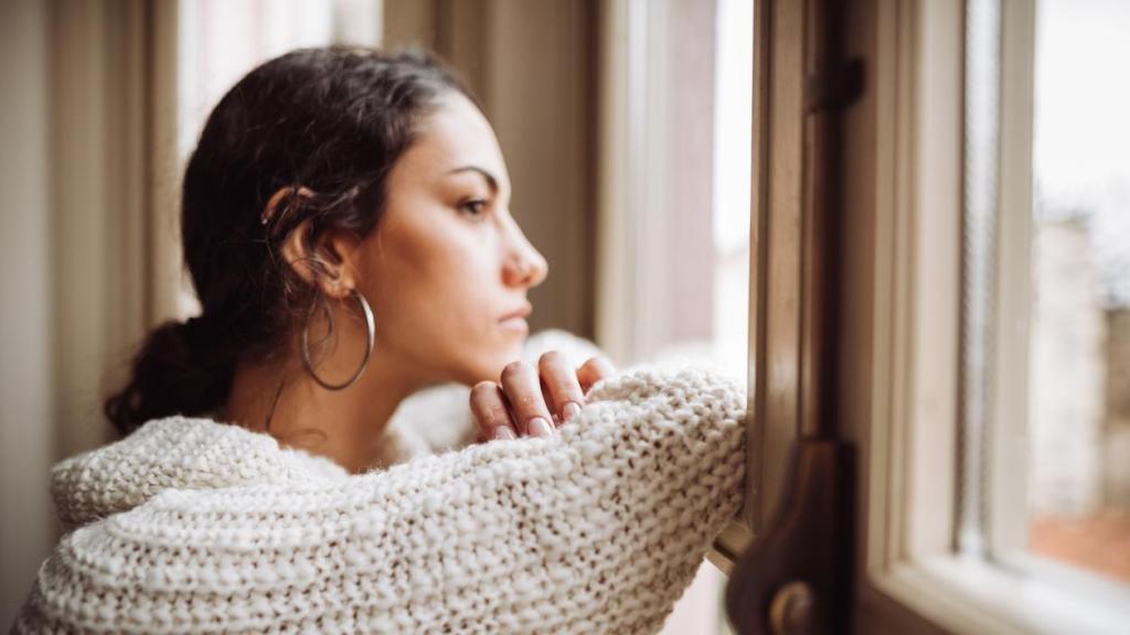 Mujer joven mirando por la ventana con aspecto serio.