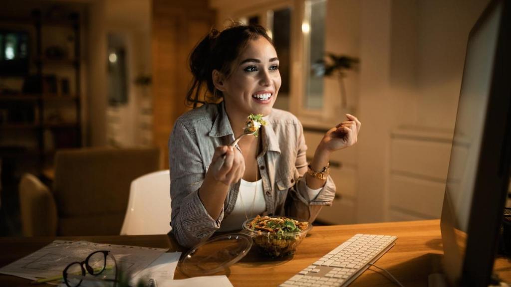 Mujer cenando una ensalada frente al ordenador.