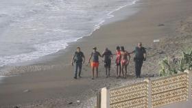 Dos guardias civiles escoltan a cuatro jóvenes migrantes llegados a nado a la playa del tarajal en Ceuta.