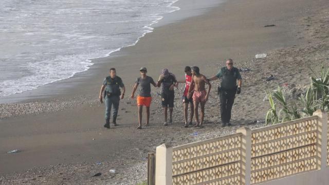 Dos guardias civiles escoltan a cuatro jóvenes migrantes llegados, este martes, a nado a la playa del tarajal en Ceuta.