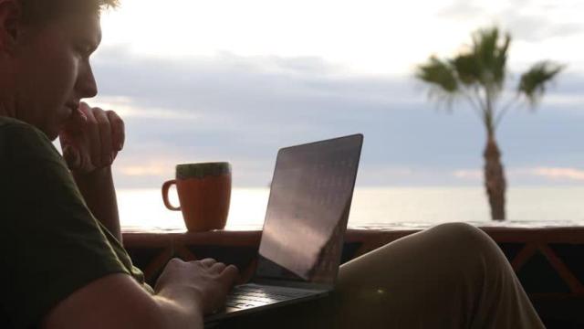 Un hombre teletrabajando cerca de la playa.