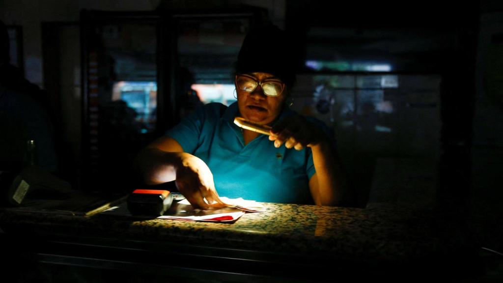 Una mujer cuenta dinero en un puesto de comida usando la luz de su teléfono móvil durante un corte de energía que afecta a Caracas y otras regiones del país, en Caracas, Venezuela, el 30 de agosto de 2024.