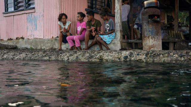 Unos niños descansan tras frente a su casa en Fiji cuando la marea sube hasta inundar su calle.