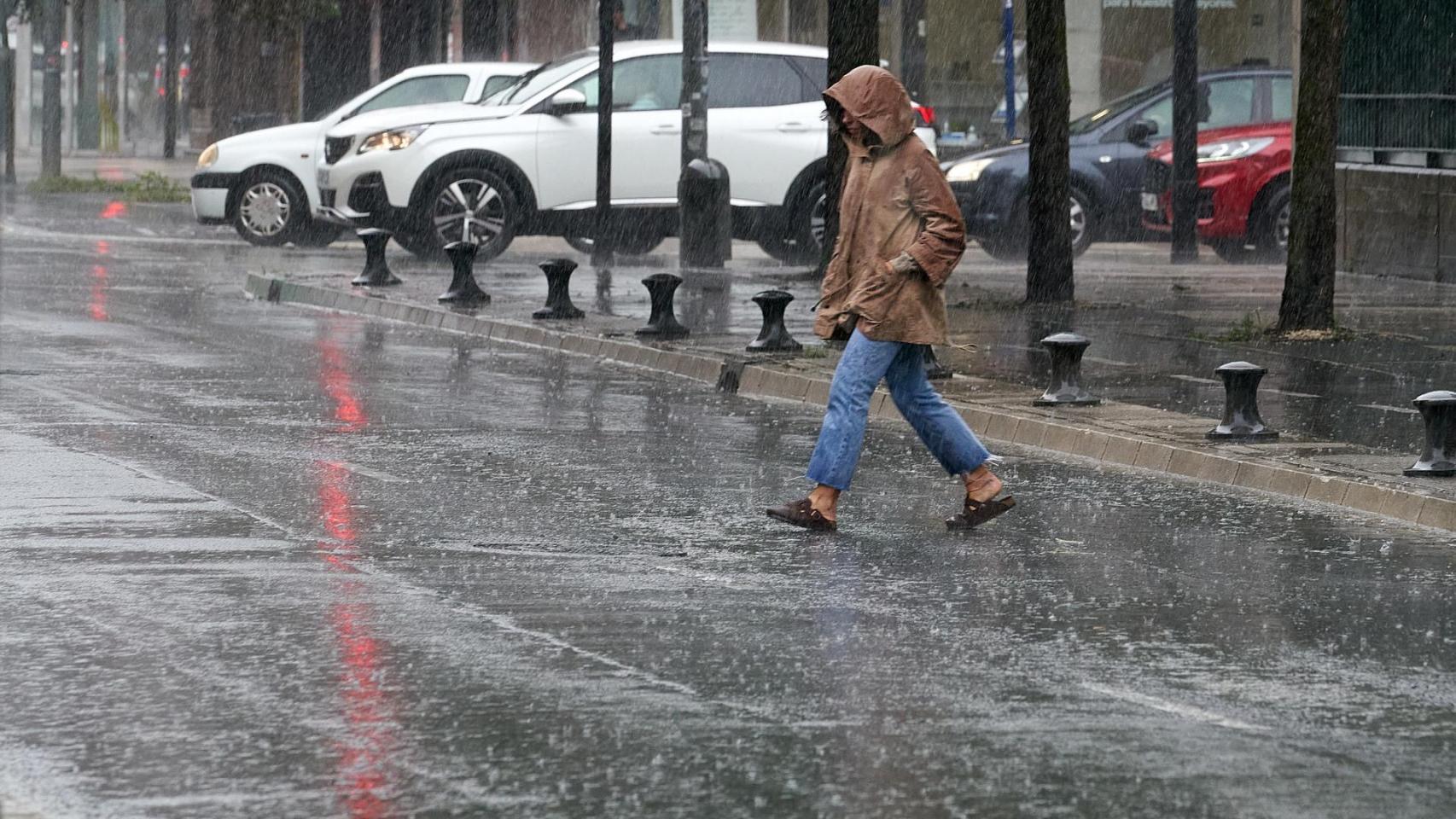 Una persona cruza la calle bajo la lluvia.