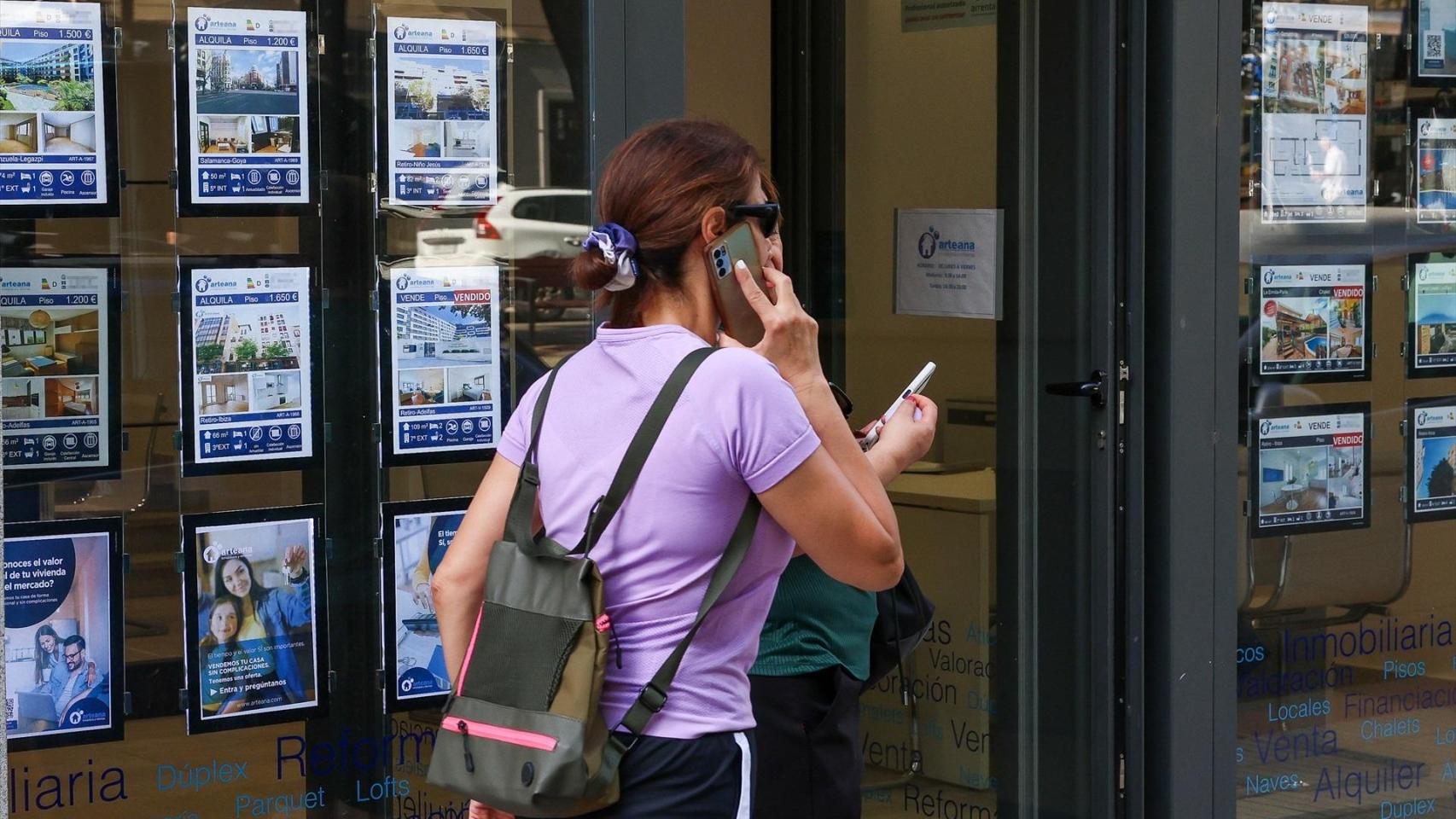 Una joven pasa por delante del escaparate de una inmobiliaria.