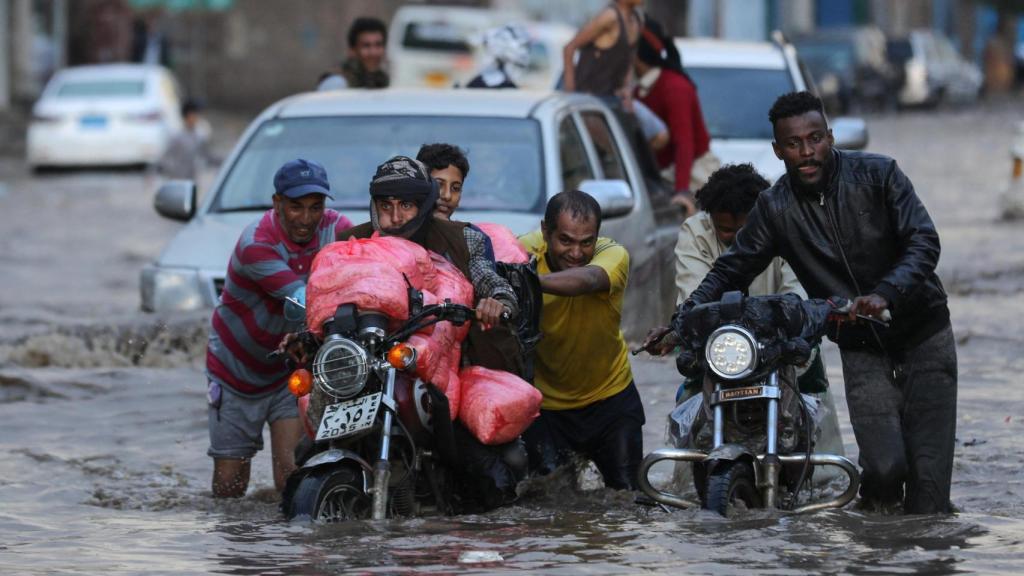 La gente empuja motocicletas en una calle inundada durante las fuertes lluvias en Sanaa, Yemen, 25 de agosto de 2024.