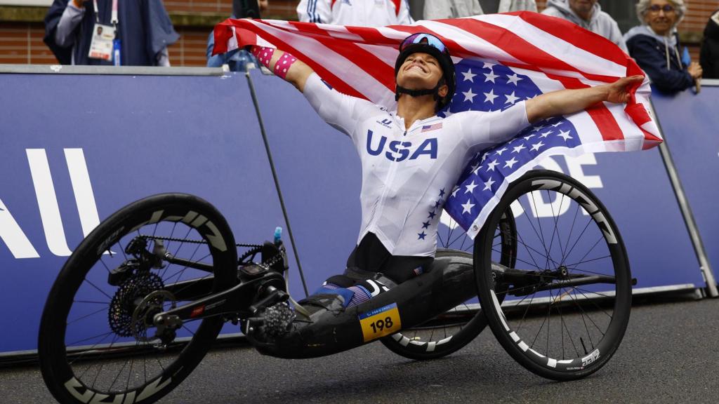 Oksana Masters celebra una victoria en handbike con la bandera de Estados Unidos.