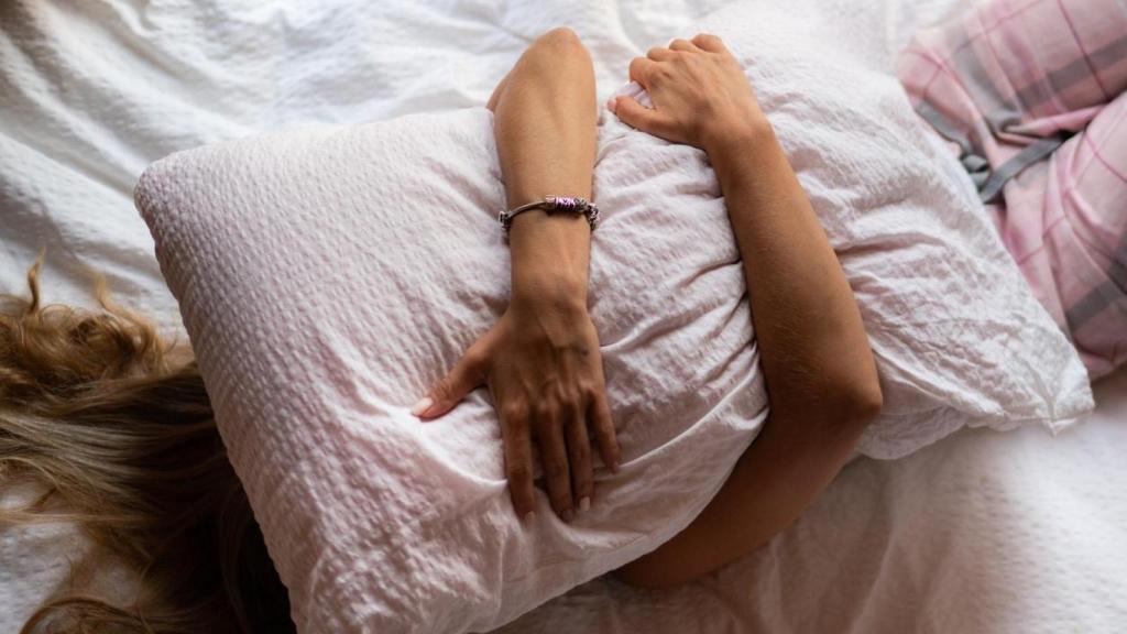 Mujer en la cama abrazando una almohada.