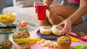 Una mujer comiendo donuts y comida poco saludable.