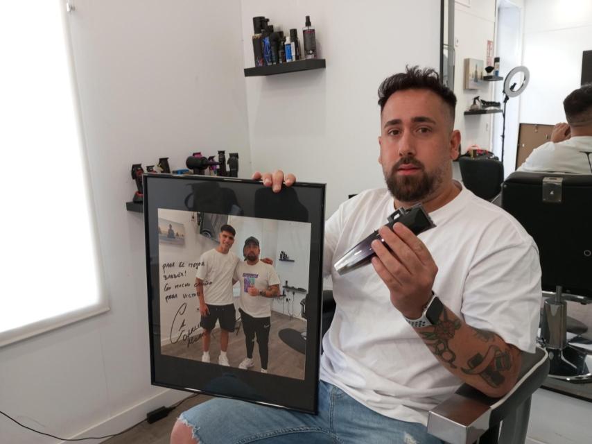 Víctor Manuel Martínez Marín, este lunes, posando con el autógrafo que tiene de Carlos Alcaraz en su barbería de El Palmar.