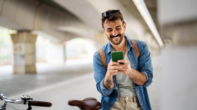 Persona sonriente escribiendo en el teléfono y de pie con su bicicleta.