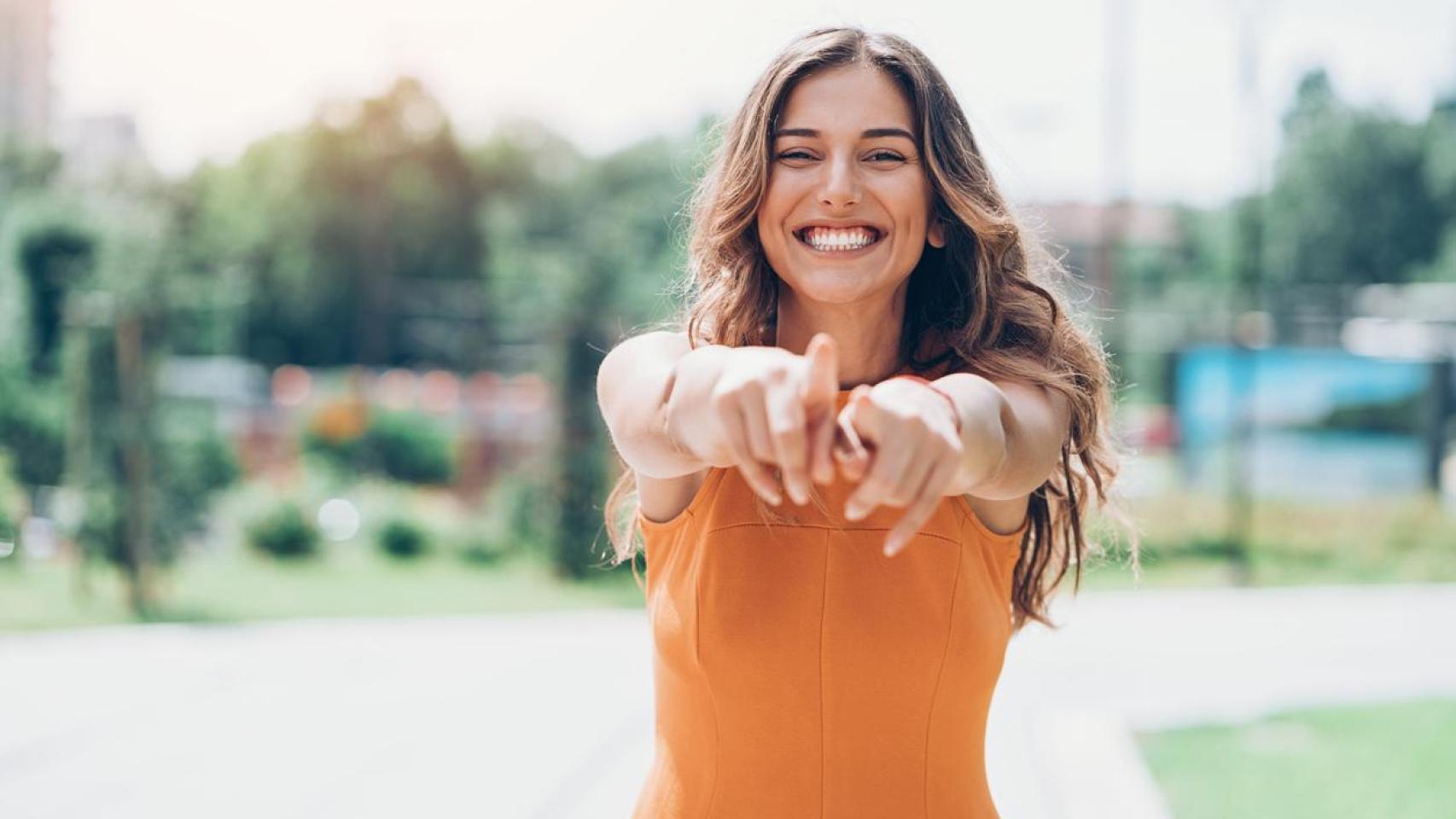 Mujer sonriendo y señalando a la cámara.