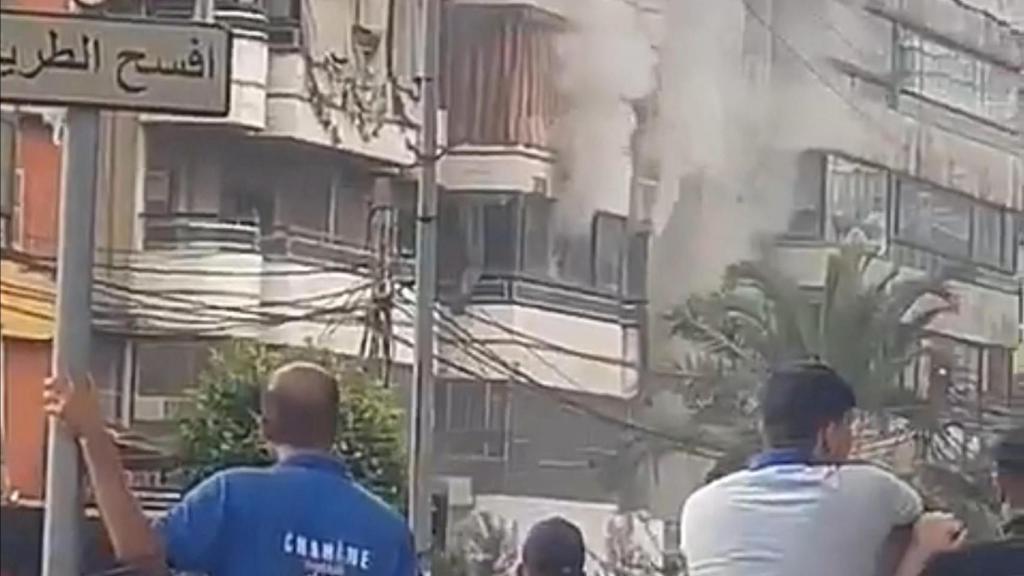 La gente observa cómo sale humo de un edificio tras una explosión, mientras las radios portátiles utilizadas por Hezbolá detonan en el sur del Líbano y en los suburbios de Beirut.