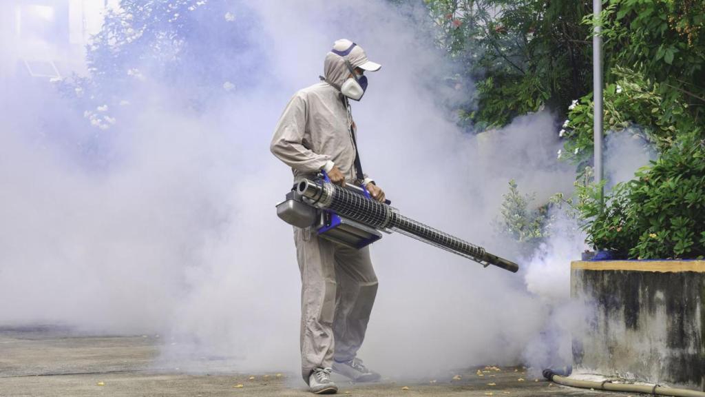 Trabajador fumigando una zona al aire libre.