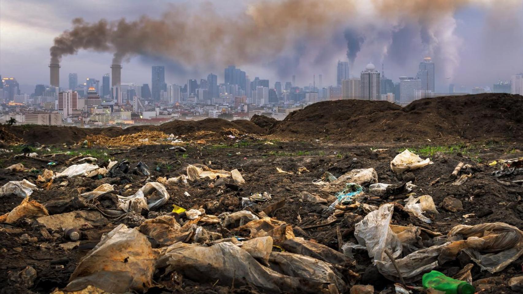 Panorámica de la basura en un campo con el fondo de la contaminación de una ciudad.