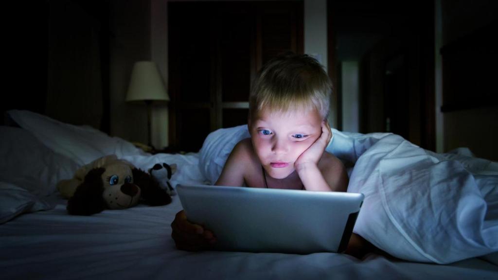 Niño jugando con una tablet durante la noche.