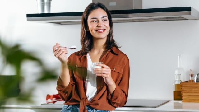 Mujer comiendo yogur en la cocina.