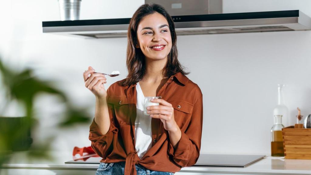 Mujer comiendo yogur en la cocina.