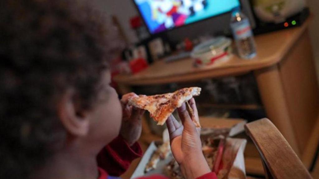 Un niño come una pizza mientras ve la televisión.