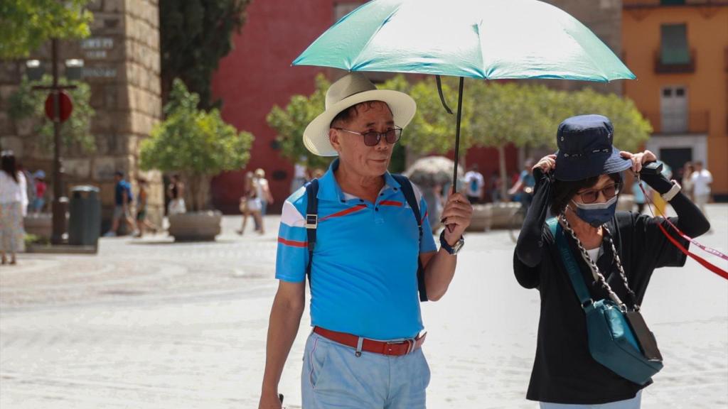 Unos turistas tratan de resguardarse del sol mediante sombreros y paraguas