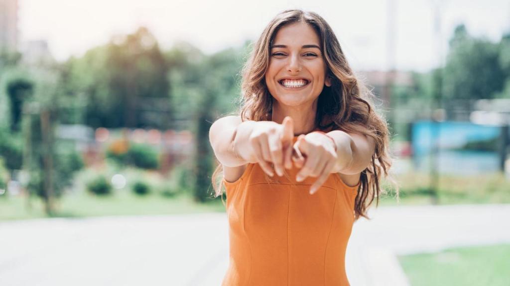 Mujer sonriendo señalando a la cámara.