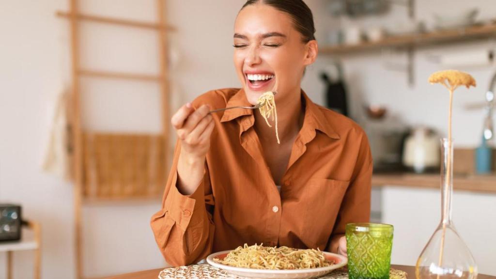 Mujer sonriente comiendo pasta.