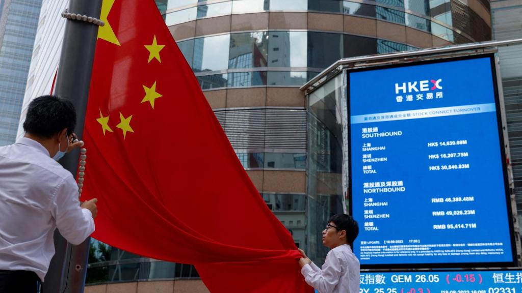 Dos personas despliegan una bandera de China frente a un monitor donde se recoge la evolución de la Bolsa de Hong Kong.