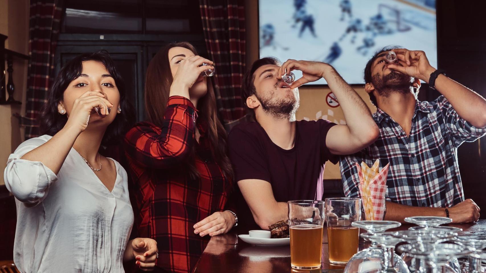 Cuatro jóvenes beben chupitos en la barra de un bar.