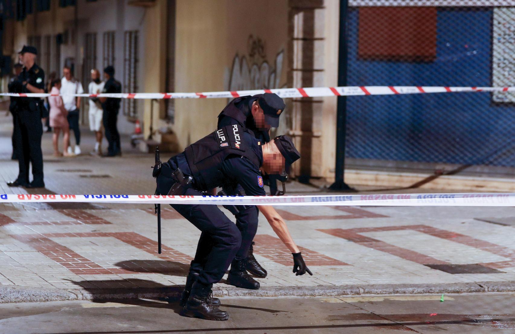 Agentes de policía señalan un charco de sangre en el lugar en el que se ha producido un tiroteo en el que varias personas han resultado heridas este sábado por la tarde en Málaga capital.