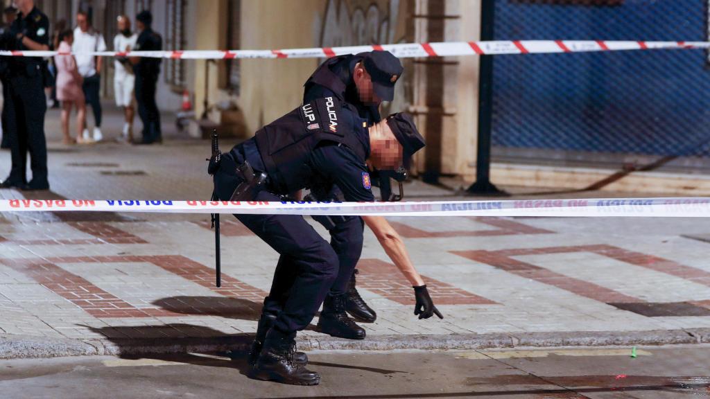 Agentes de policía señalan un charco de sangre en el lugar en el que se ha producido un tiroteo en el que varias personas han resultado heridas este sábado por la tarde en Málaga capital.