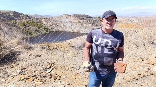 Antonio Fernández, arqueólogo, muestra dos rocas procedentes de la minería frente al lago rojo de La Unión.