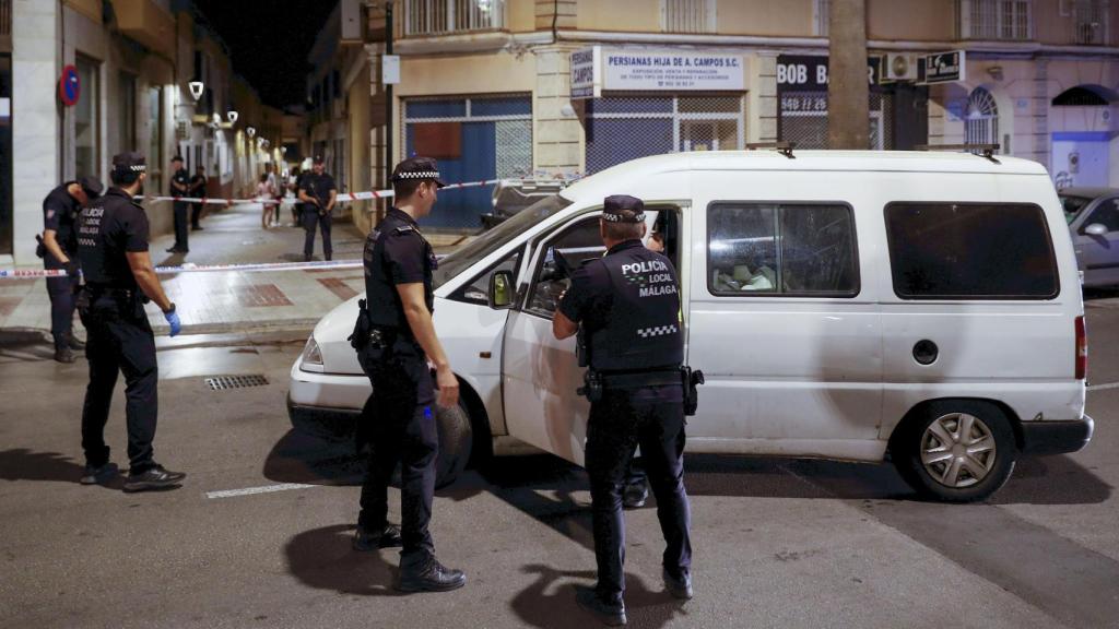 Agentes de policía retiran el coche que ha recibido varios impactos de bala en el lugar en el que se ha producido un tiroteo en el que varias personas han resultado heridas este sábado por la tarde en Málaga capital.