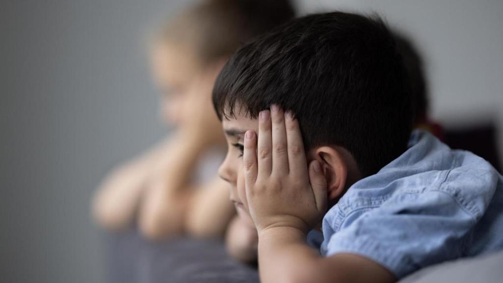 Niños pequeños pensativos en el sofá de una casa.