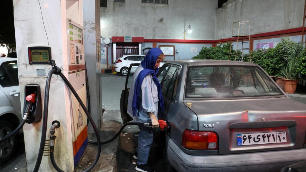 Una mujer iraní llena el tanque de combustible de su automóvil en una gasolinera, después del ataque del CGRI a Israel, en Teherán.