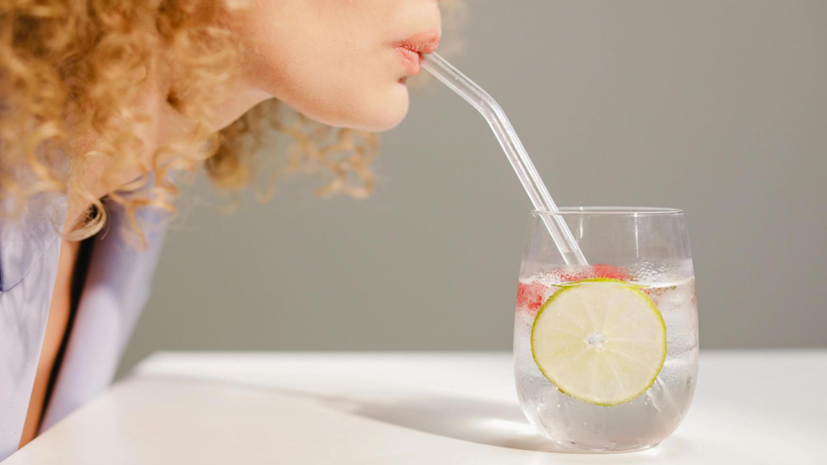 Mujer bebiendo agua de un vaso con pajita