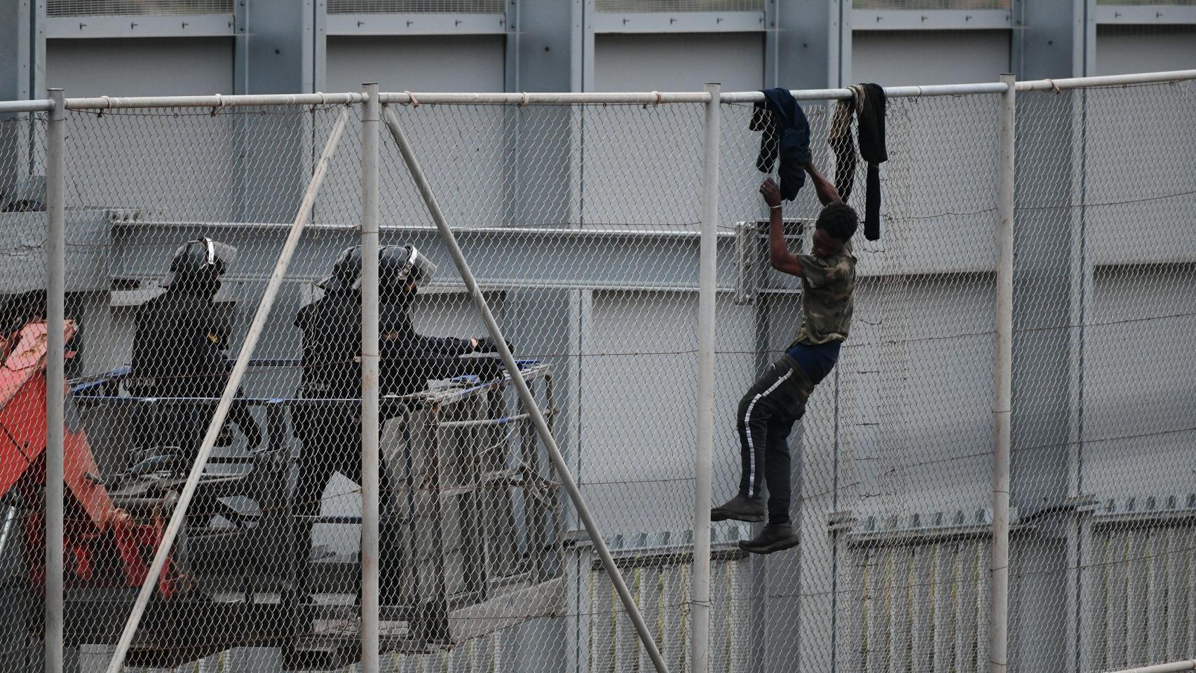 Dos agentes se acercan a un migrante que intenta saltar la valla que separa Ceuta de Marruecos.