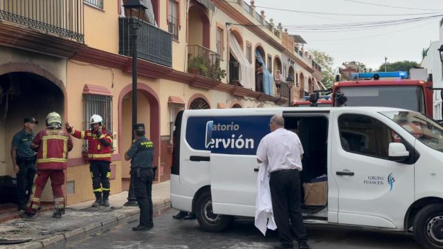 Bomberos, Guardia Civil y servicios funerarios trabajan a las puertas de la vivienda incendiada en Guillena.