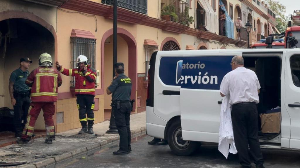 Bomberos, Guardia Civil y servicios funerarios trabajan a las puertas de la vivienda incendiada en Guillena.