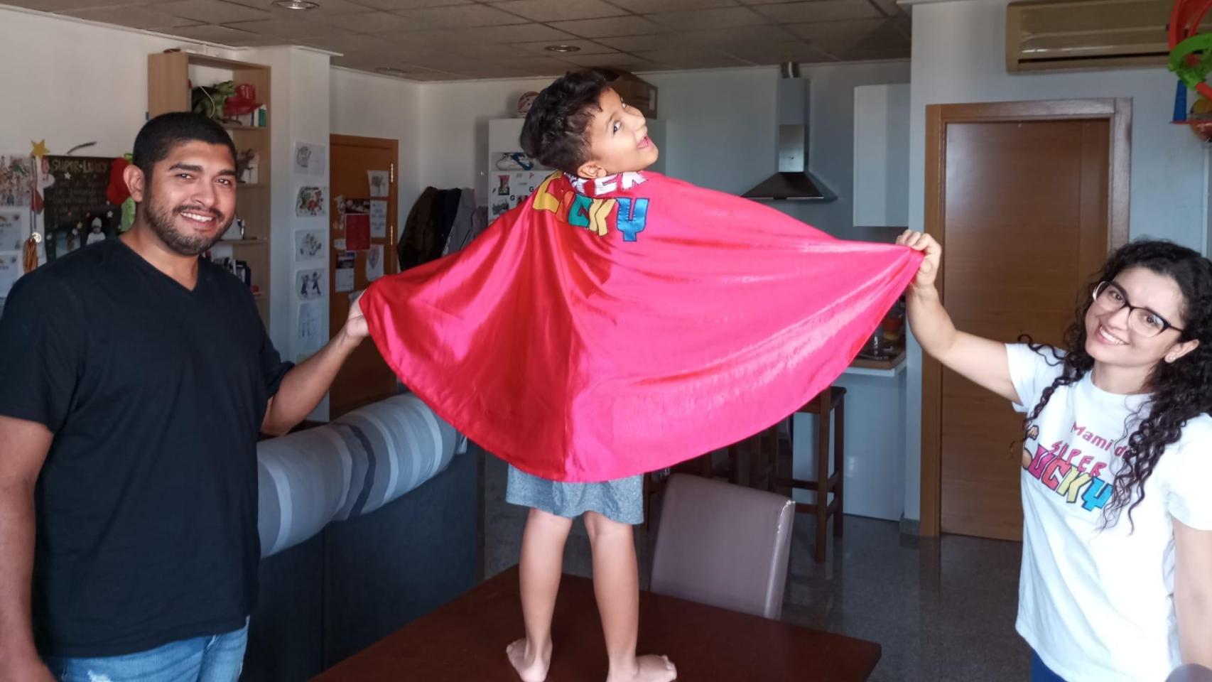 José y su pareja, Tatiana,  este viernes, sujetando la capa de Super Lucky, en su piso de Molina de Segura, mientras sonríe el pequeño Luciano subido a la mesa del comedor.